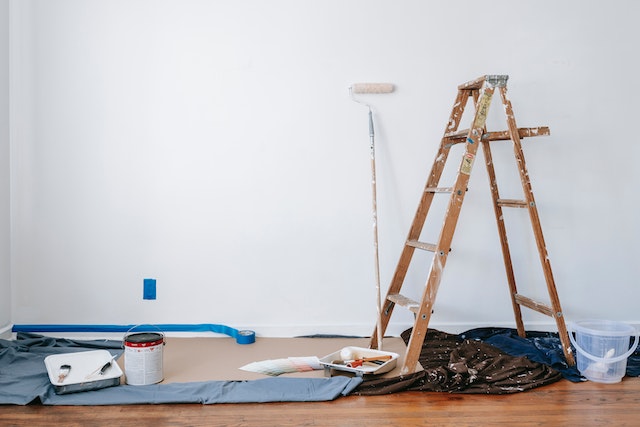 a ladder, tarp and paint supplies in front of a blank wall